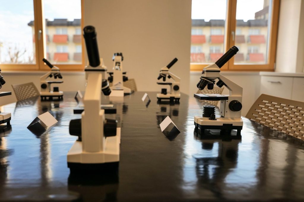 Laboratório de ensino moderno com microscópios dispostos sobre uma bancada e amplas janelas ao fundo.